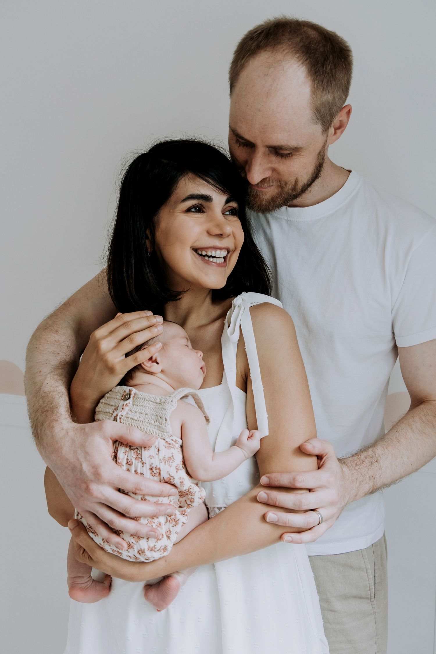 Parents smiling while holding their sleeping newborn baby during an in-home lifestyle photography session.