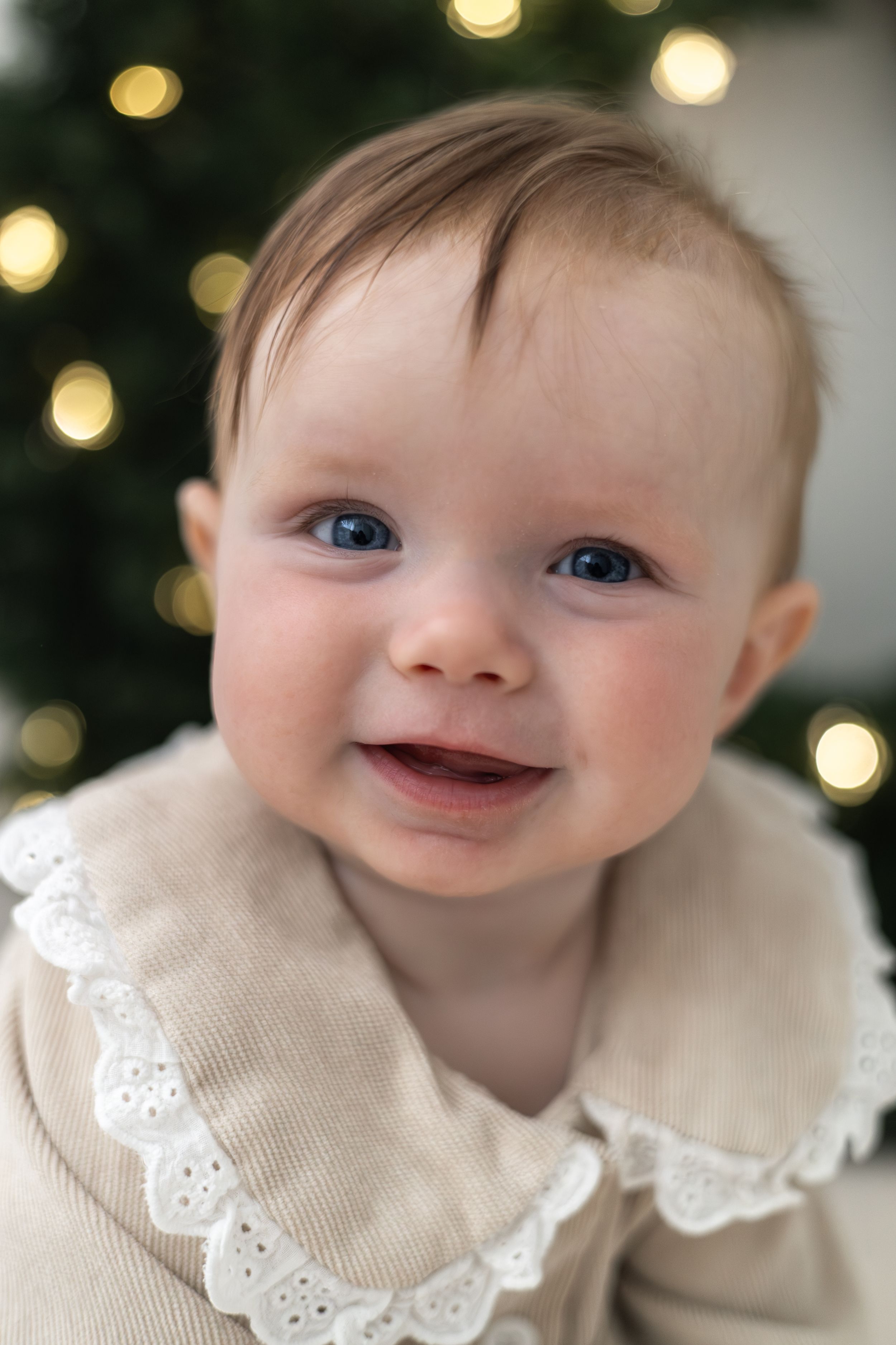 Close-up of happy baby with blue eyes smiling in front of bokeh Christmas lights Christmas mini Photoshoot Nottingham