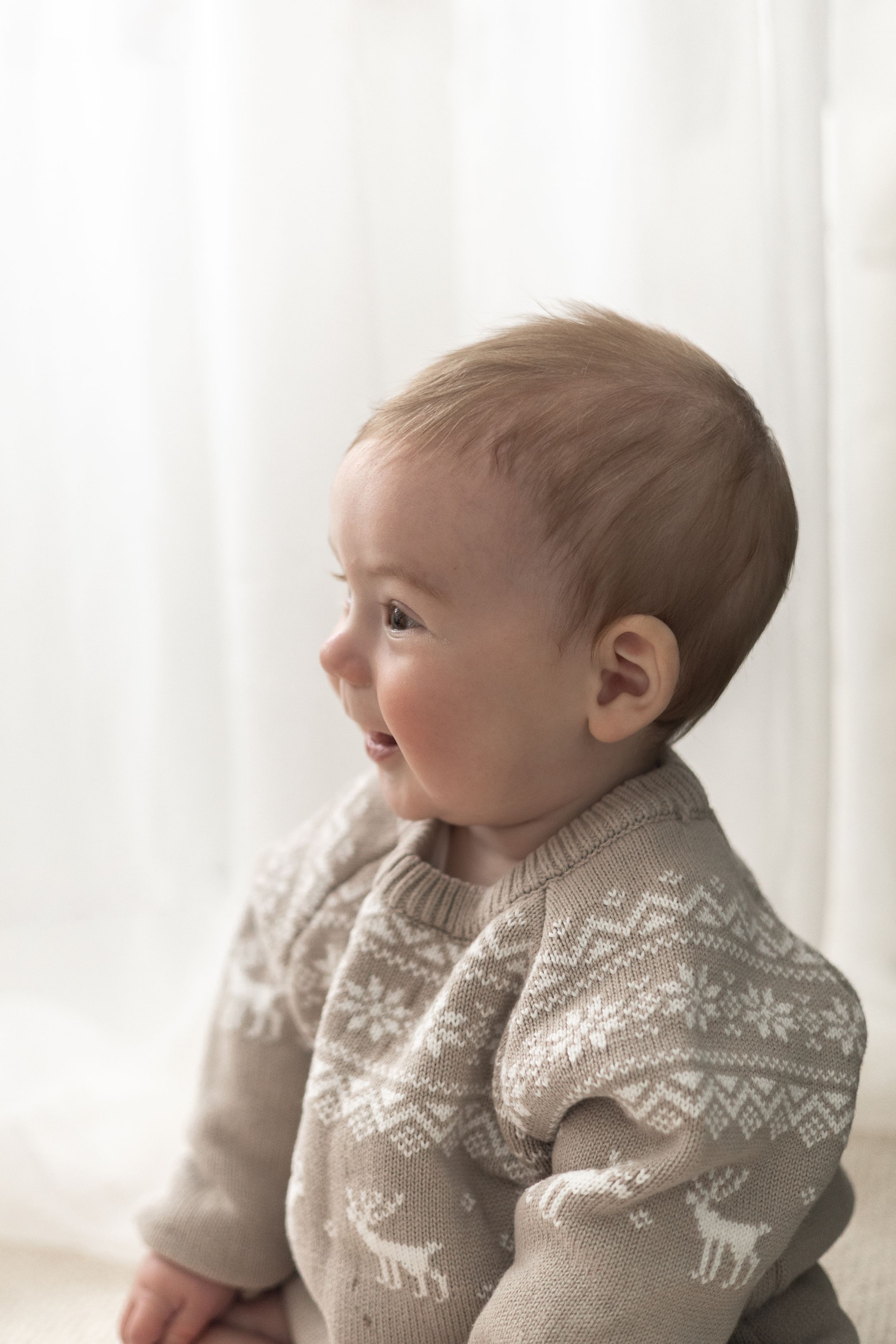 Adorable baby in a Nordic reindeer knit jumper sitting in front of a Christmas wreath Christmas mini Photoshoot Nottingham