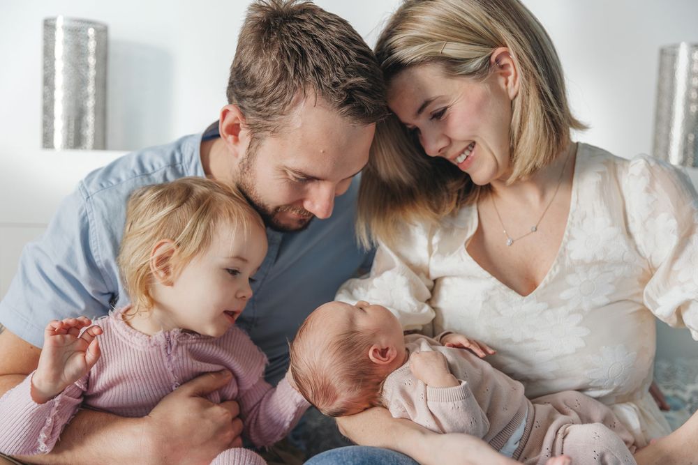 Happy young family with toddler girl and newborn baby bonding together in a cozy bedroom setting.