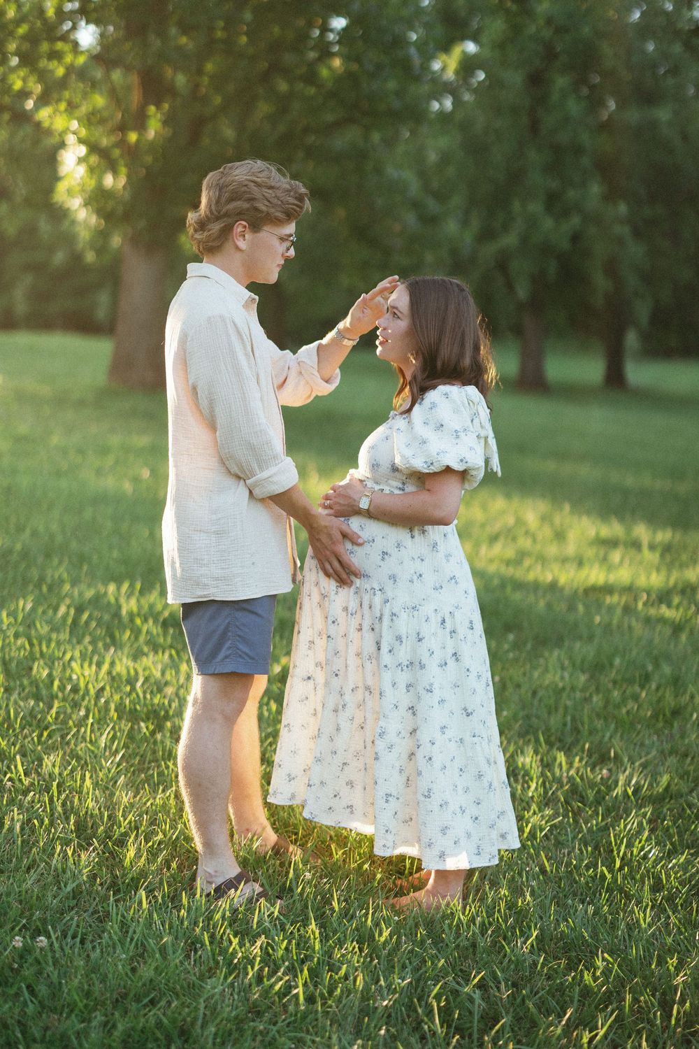 Couple sharing a tender moment on green grass, man gently touching pregnant womans face.