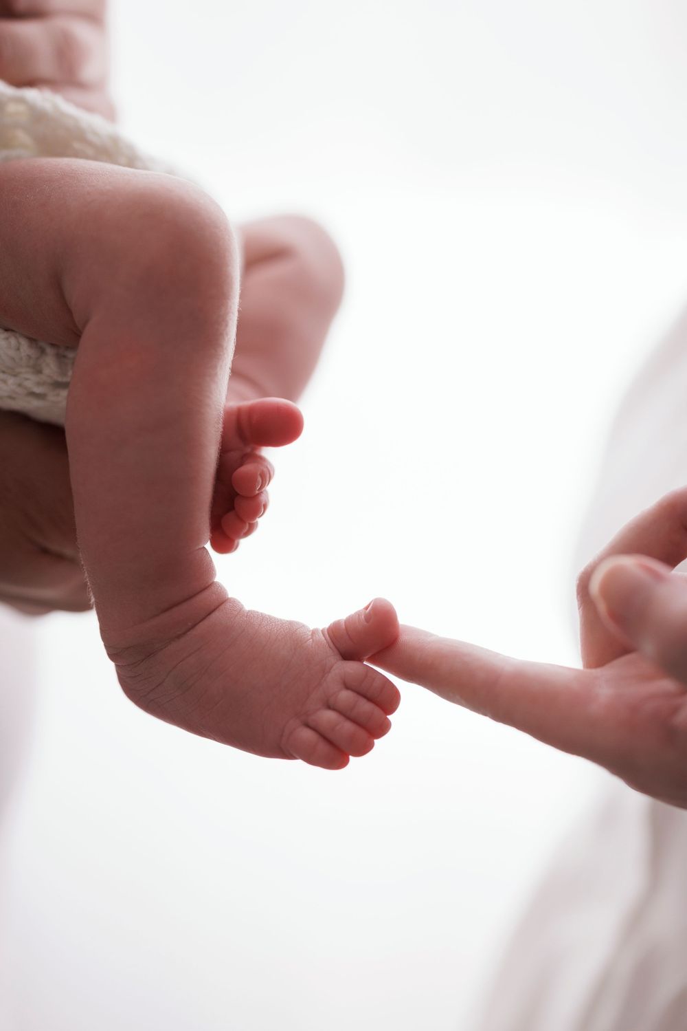 Newborn baby toes curling around an adult finger, close-up of tiny infant feet being held gently.