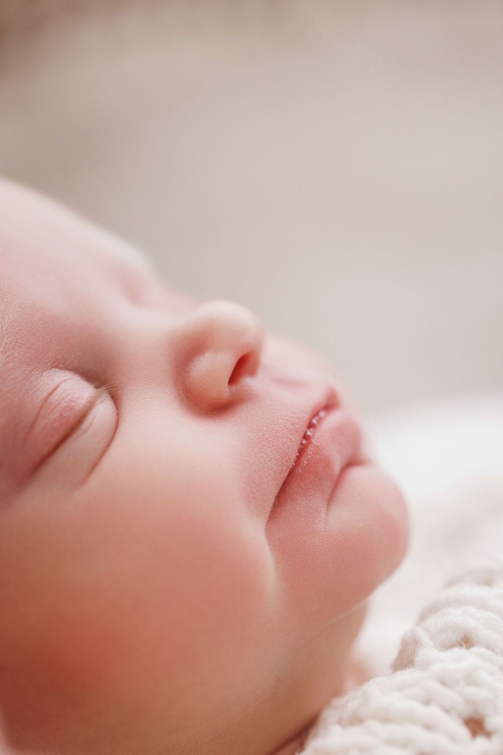Peaceful sleeping newborn baby with delicate features resting on soft white knit blanket.
