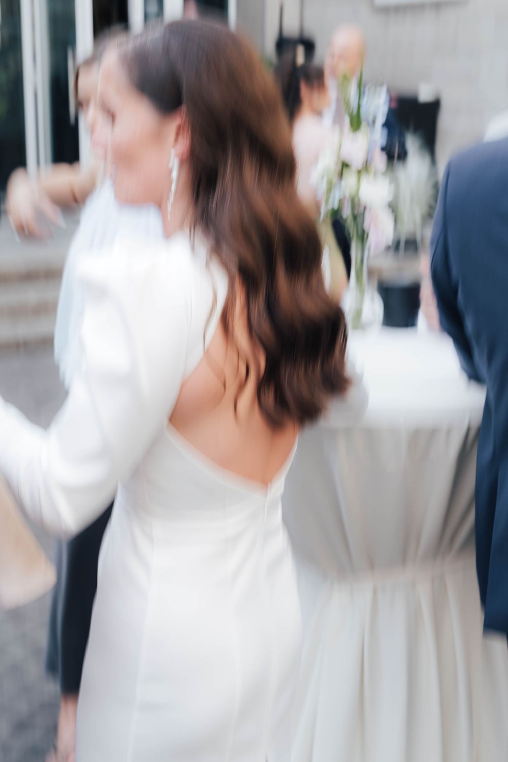 Bride in elegant backless white gown with long sleeves dancing at wedding reception.