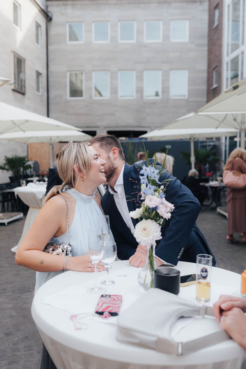 Couple sharing a romantic moment at an outdoor wedding reception table with flowers and champagne glasses.