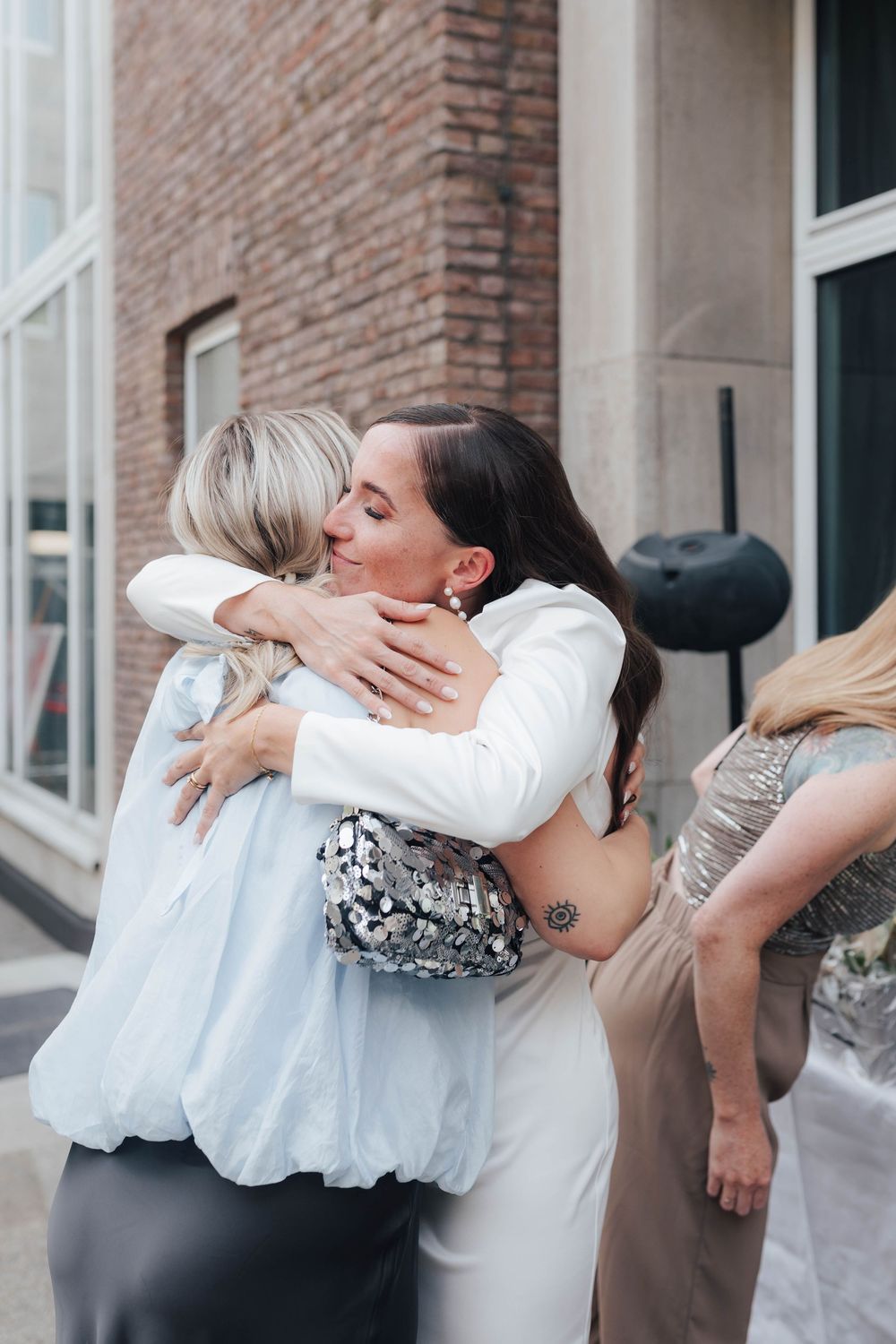 Two women sharing warm embrace at elegant outdoor wedding celebration.
