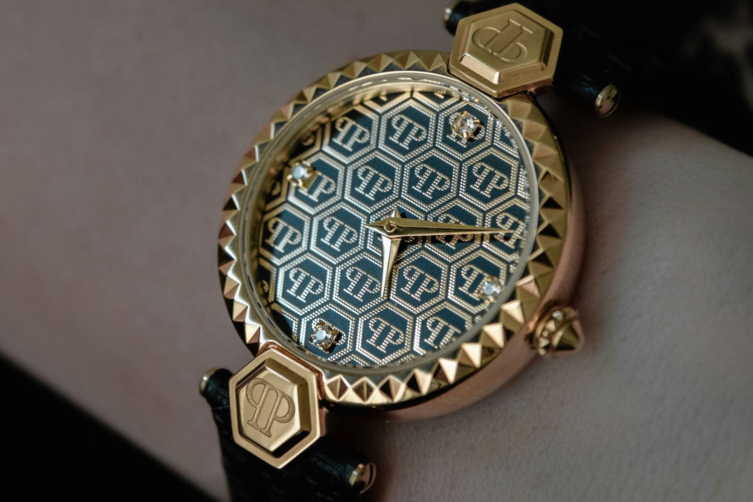 Luxury gold watch with geometric hexagon patterned blue dial and black leather strap, ornate studded bezel detail.
