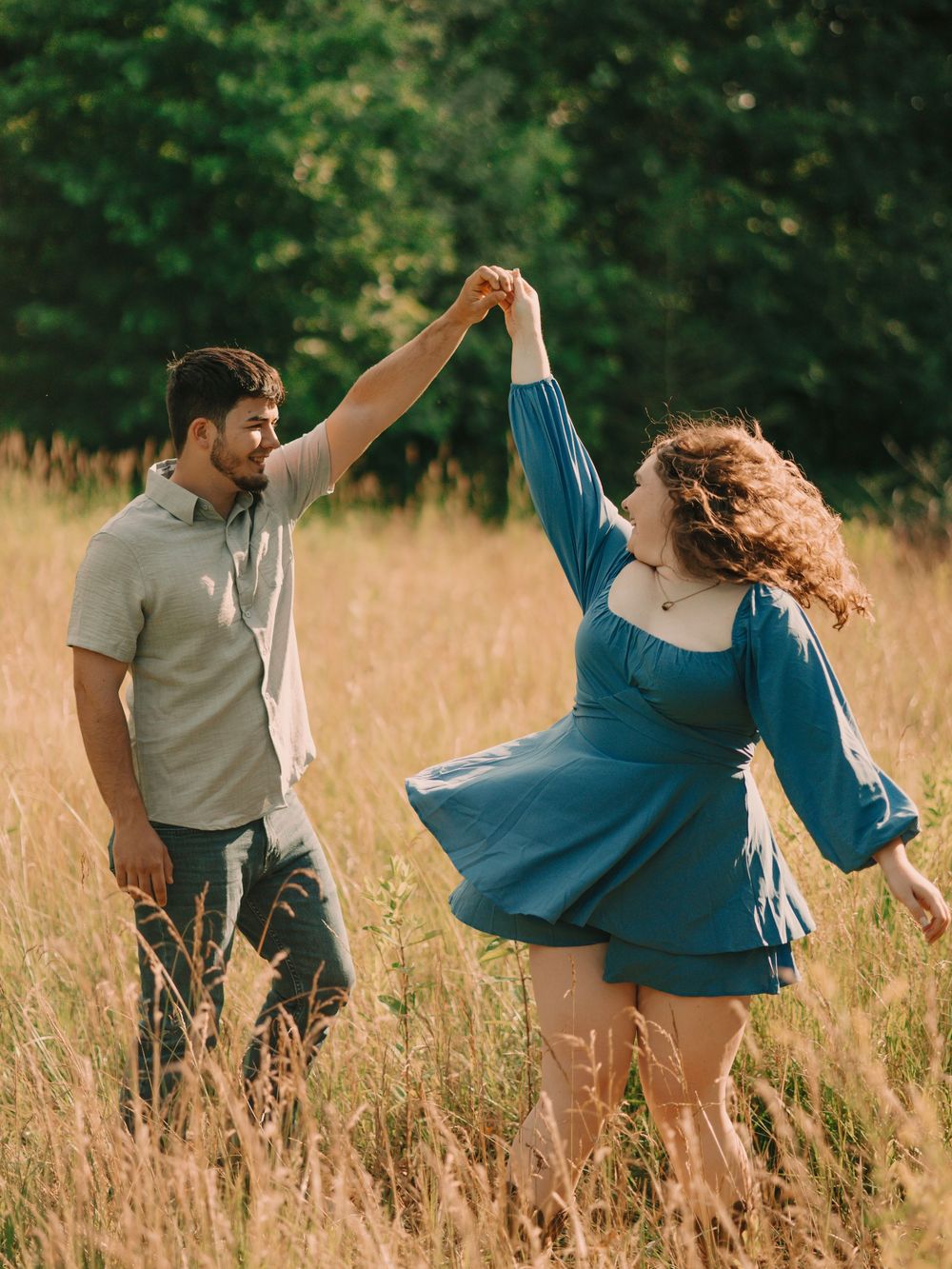 Man holding a woman's hand and spinning her around in a tall grassy field while smiling and laughing at each other