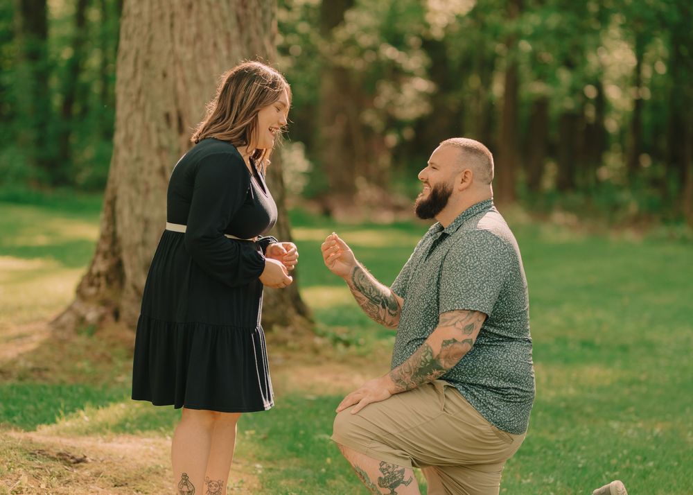 Man on one knee surprising a woman with a proposal in a grassy sun-lit field