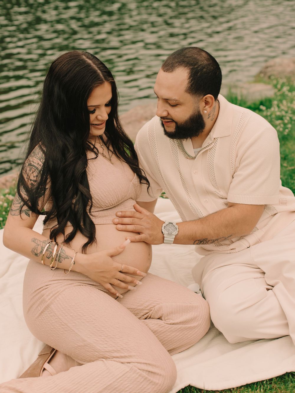 Pregnant mother and father couple near a pond with their hands on the mother's belly