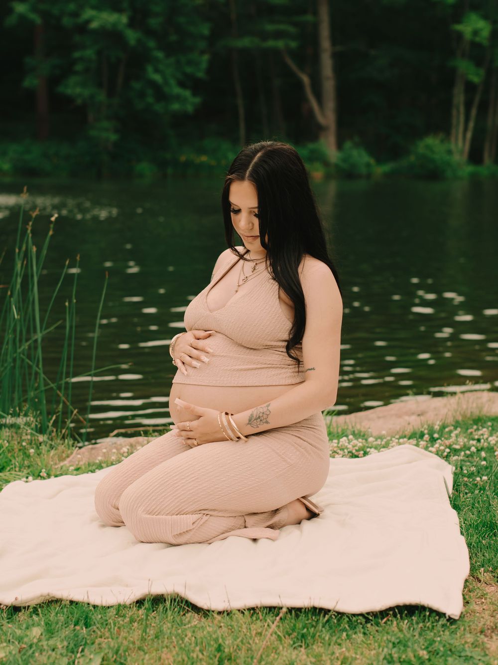 Pregnant mother holding her baby bump on the shore of a pond in the woods