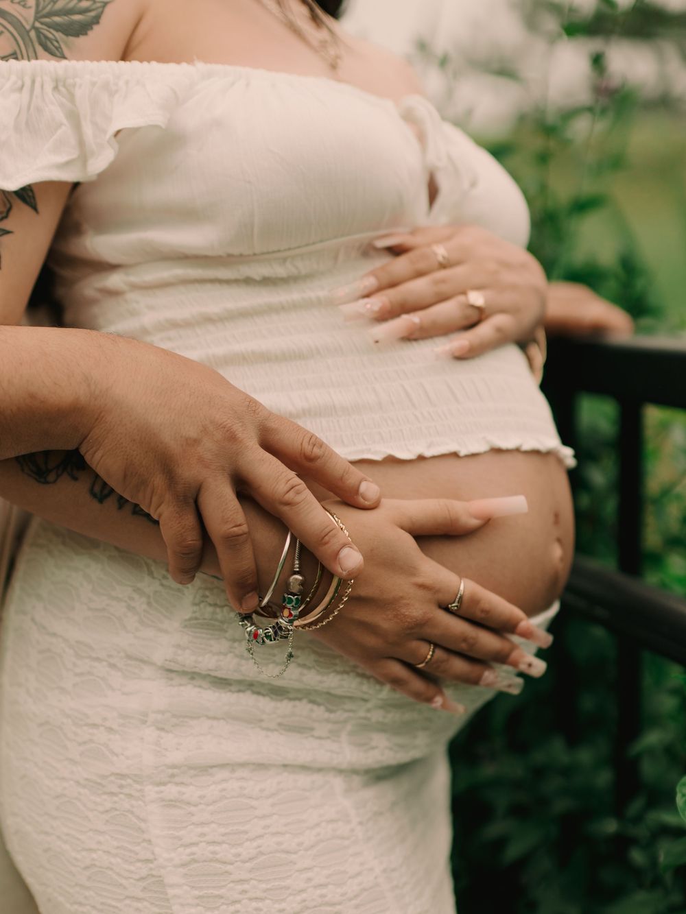 Pregnant mother and father holding baby bump from the side on a bridge in the woods