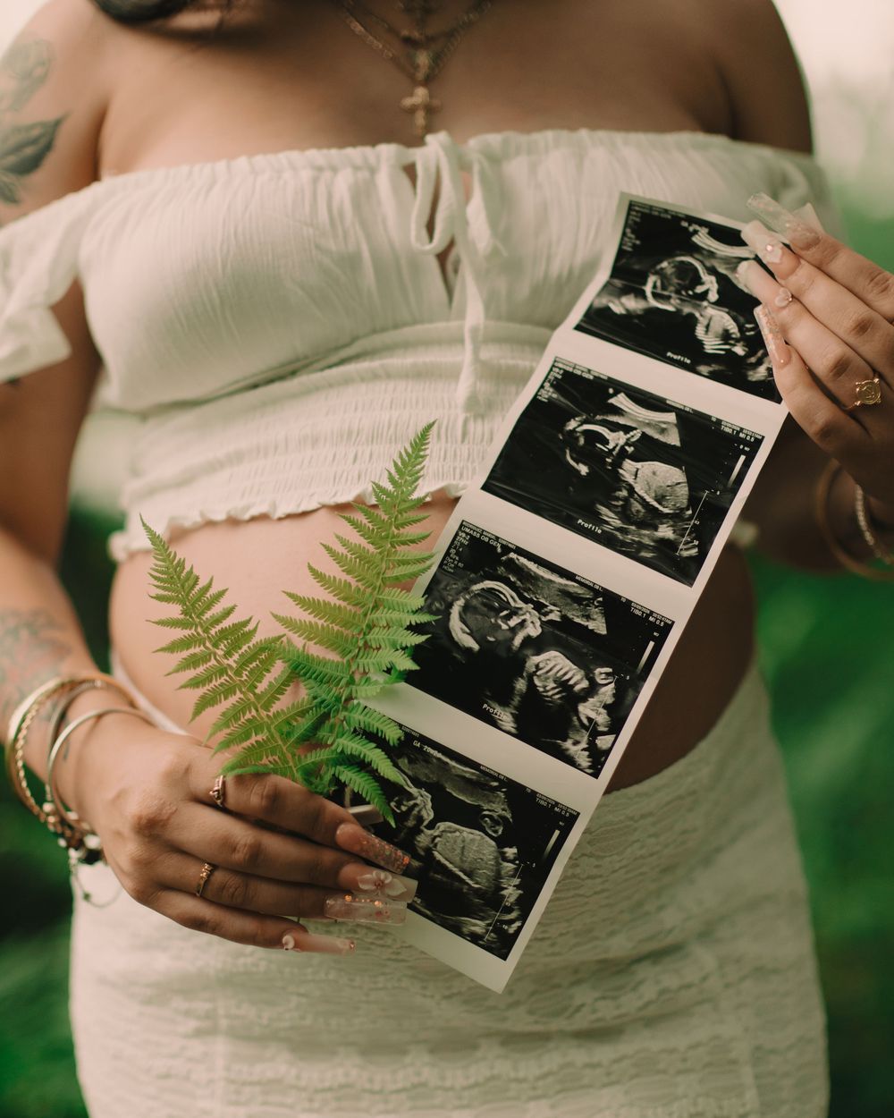 Pregnant mother holding an ultrasound with ferns in front of her baby bump outdoors in the forest