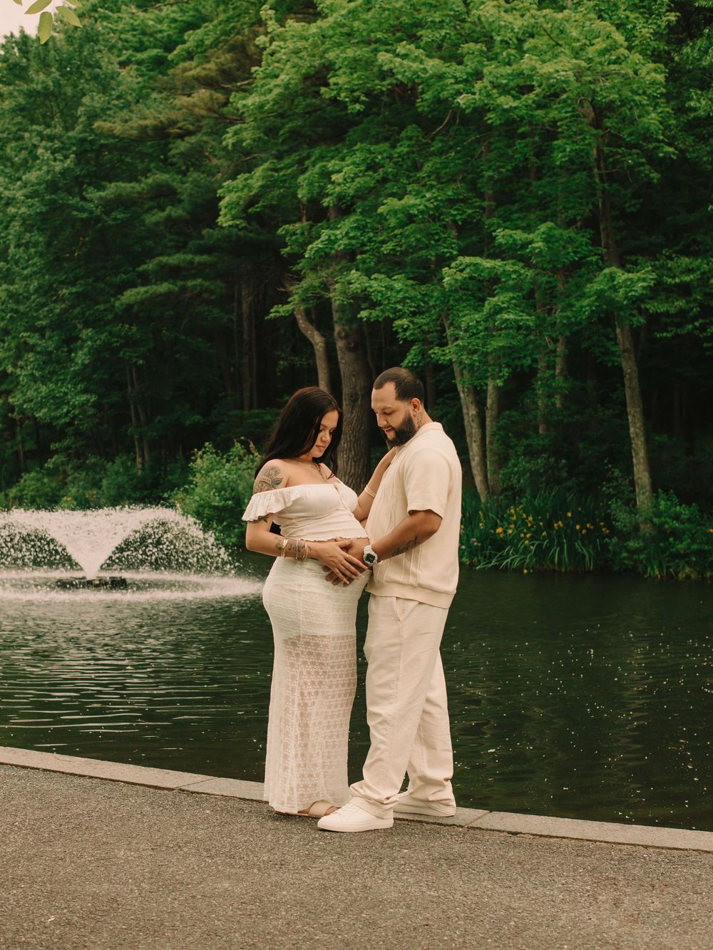 Father & pregnant mother in front of a water fountain with their hands placed on the mother's baby bump