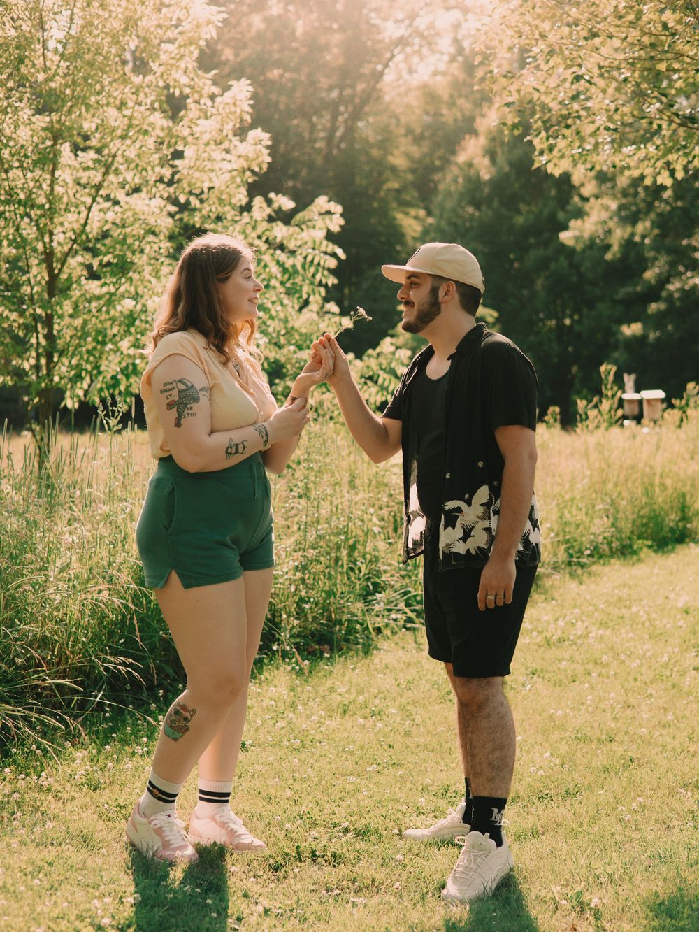 Man and woman couple standing in a sun-lit grassy field exchanging a flower