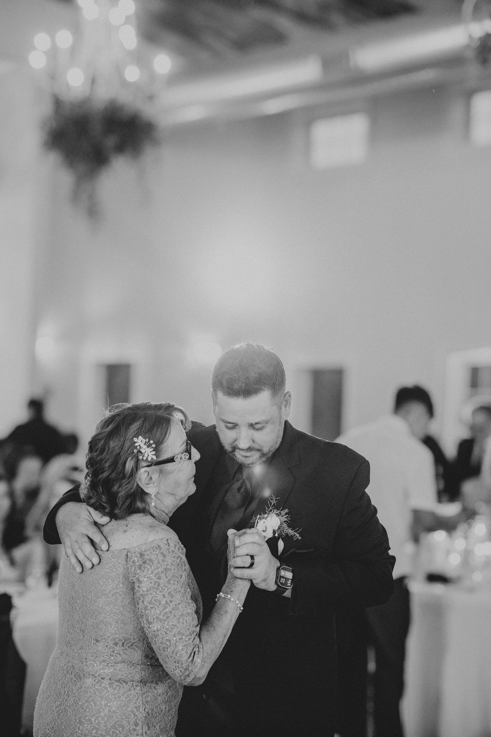 Groom shares emotional mother-son dance at wedding reception in elegant black and white photo.