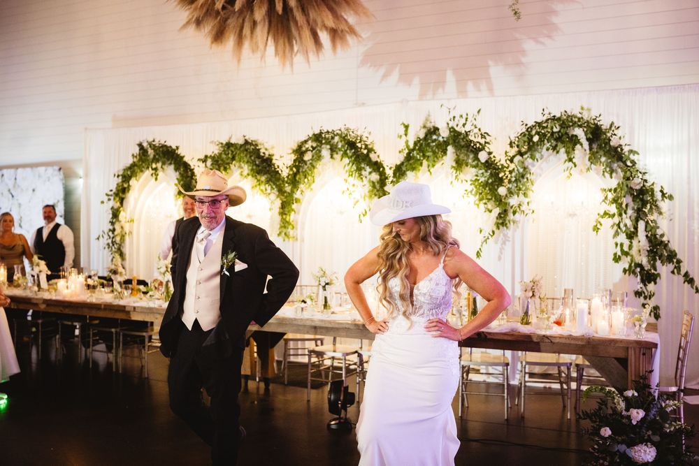 Bride and groom dancing at rustic wedding reception with heart-shaped greenery backdrop and elegant table settings.
