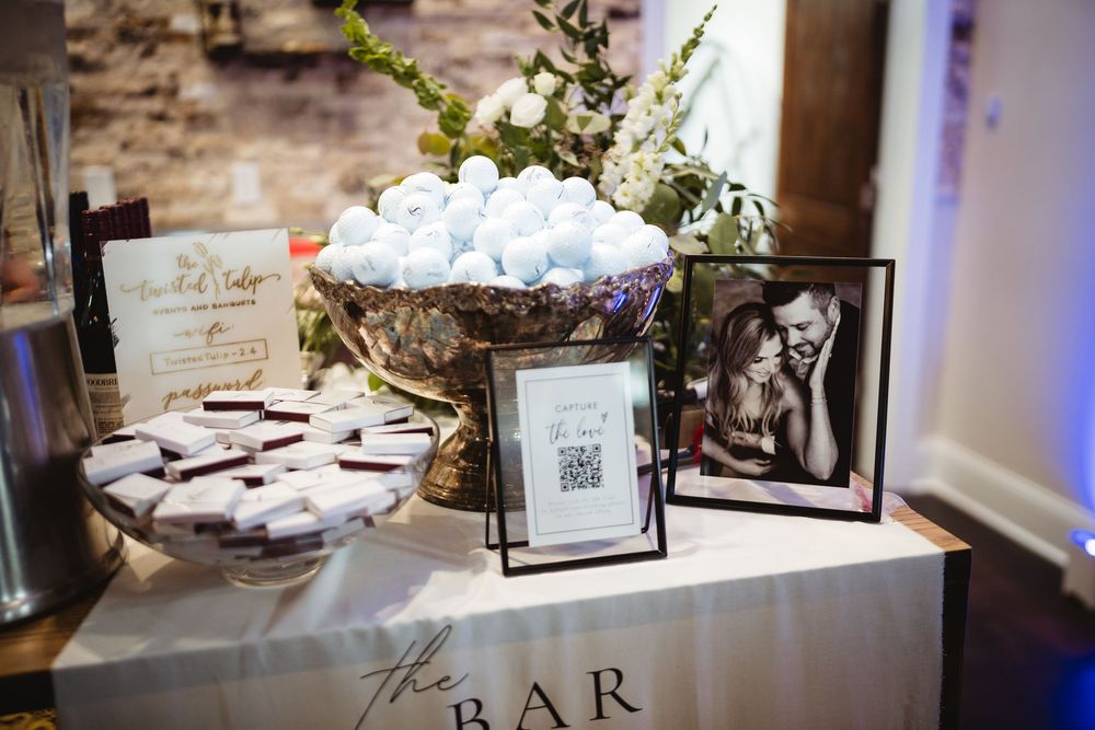 Elegant wedding bar display with white chocolate truffles, macarons, framed couple photo, and QR code sign.