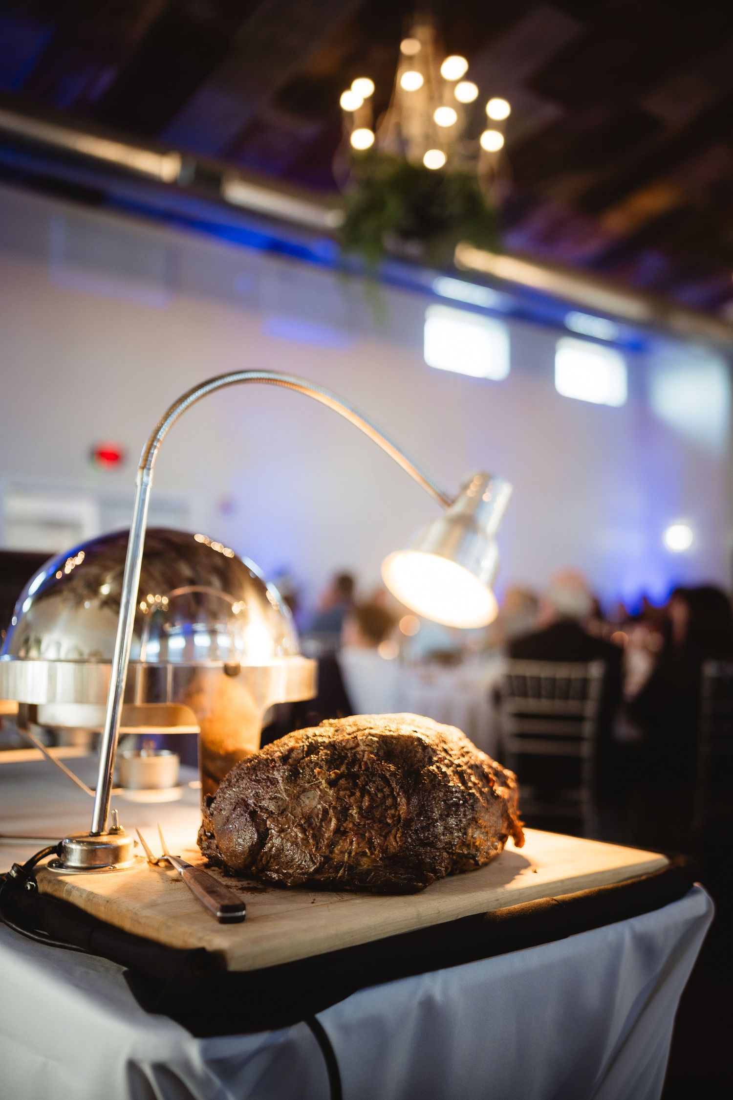 A rustic bread loaf on a wooden cutting board illuminated by a desk lamp at an elegant banquet event.