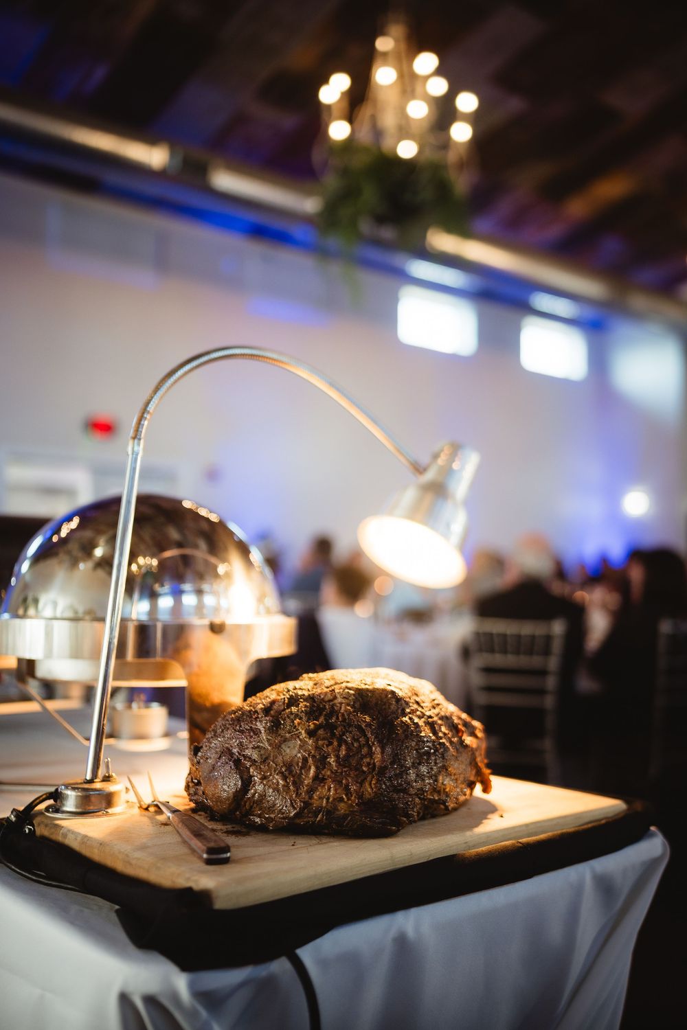 A rustic bread loaf on a wooden cutting board illuminated by a desk lamp at an elegant banquet event.