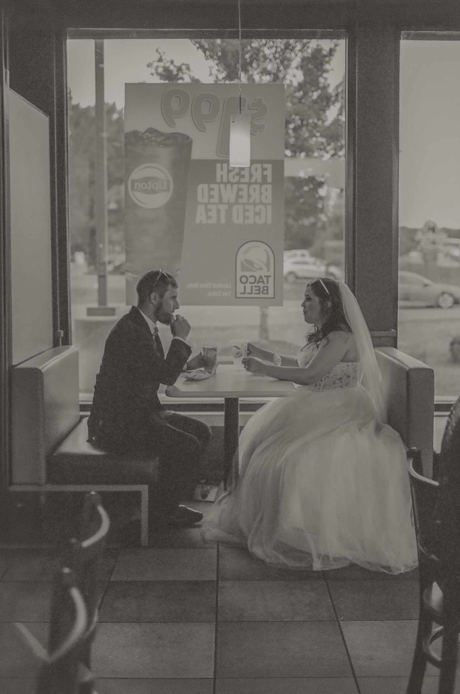Bride and groom in wedding attire sharing a meal at Taco Bell, captured in a romantic black and white photo.
