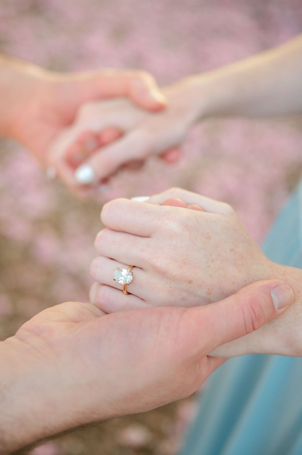 Close-up of hands holding, featuring a sparkling diamond engagement ring on a gold band.