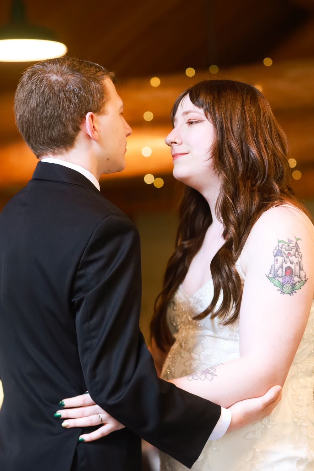 Bride and groom share an intimate moment during their first dance, bride wearing lace gown with colorful tattoo on arm.