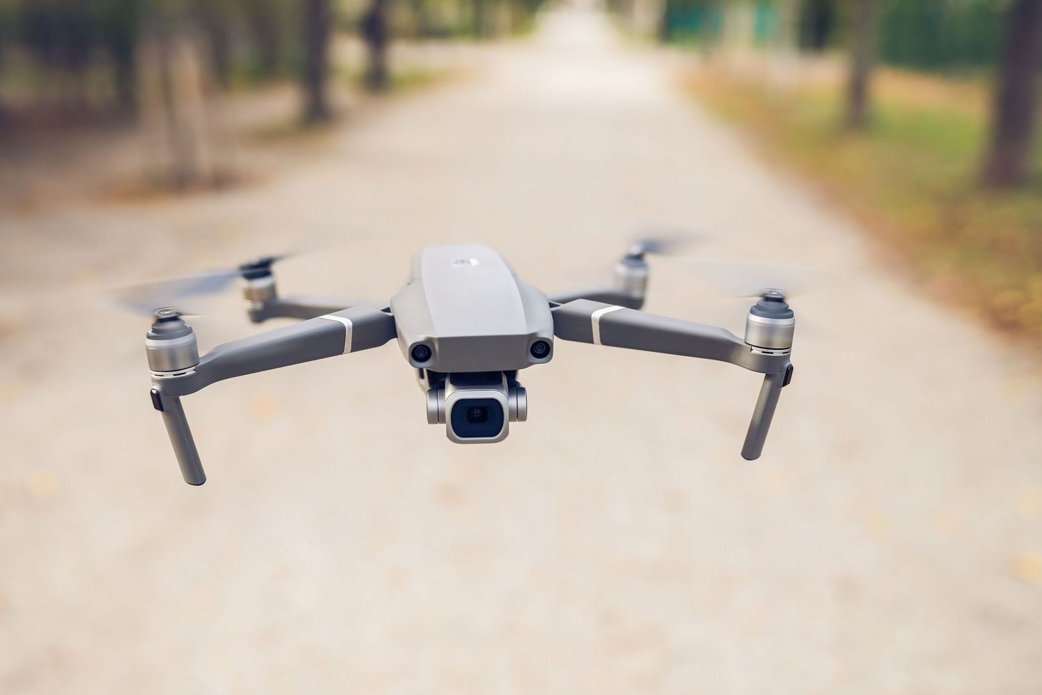 A DJI Mavic Pro 2 drone hovering mid-air on a blurred forest path background.