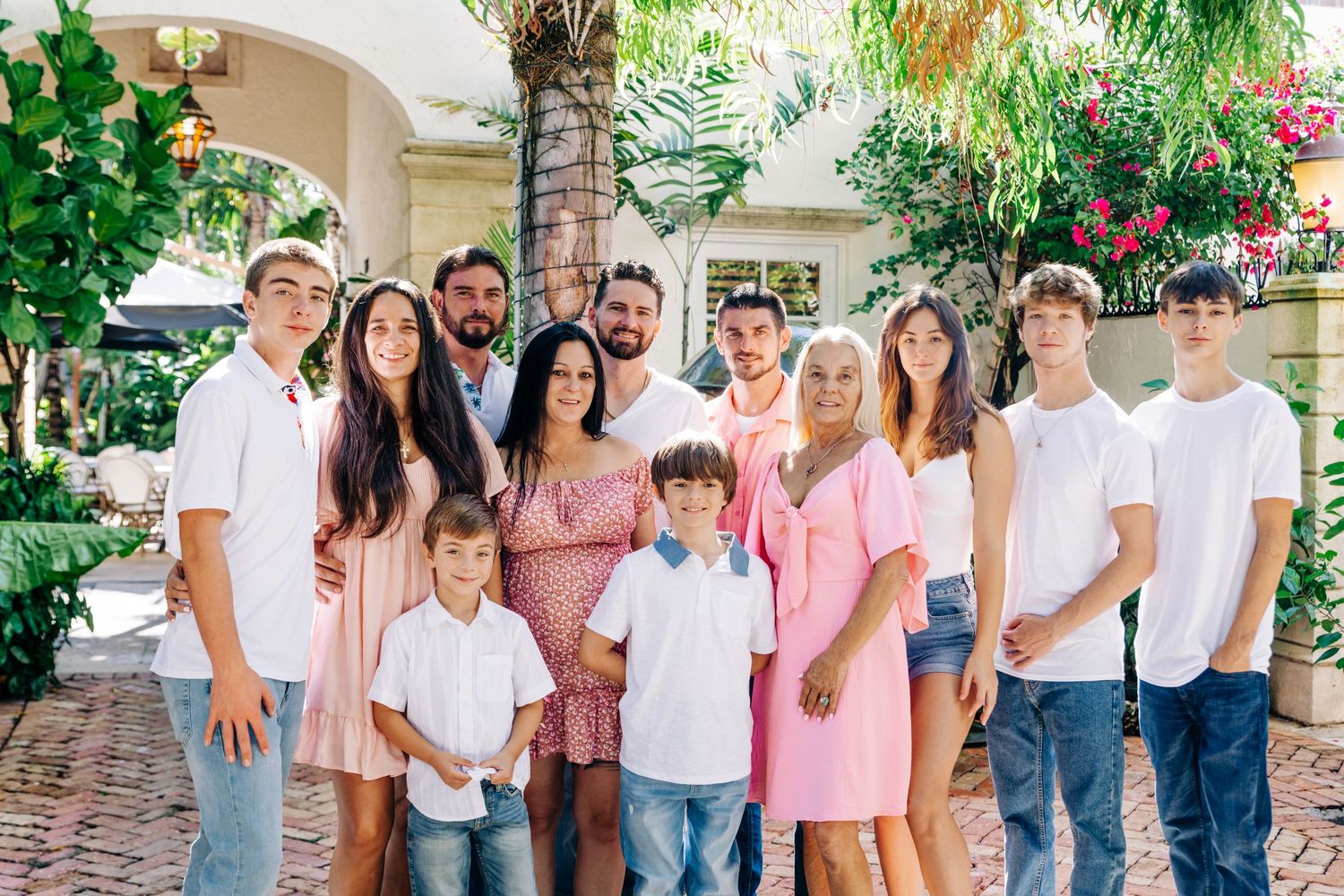 Large family group portrait outdoors near tropical garden and brick patio, smiling together in coordinated outfits in the vias of worth ave