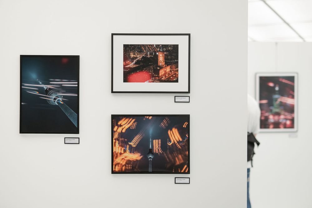 Art gallery wall displaying three framed aerial city night photography prints with vibrant red and orange lighting.
