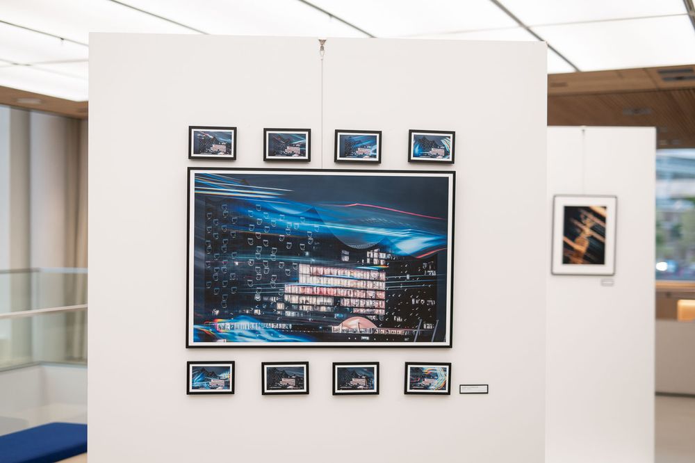 Art gallery display featuring a large cityscape night photography print surrounded by smaller framed photos on a white wall.