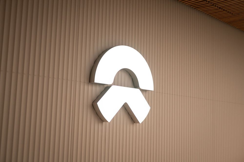White NIO electric vehicle brand logo mounted on a textured beige wall with wooden ceiling accent.