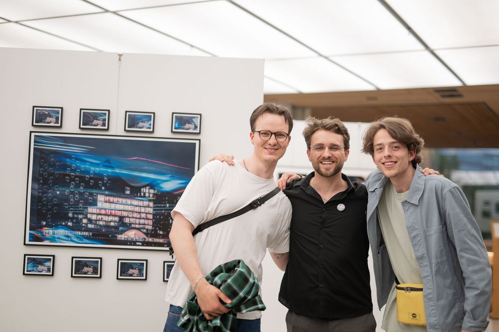 Three men smiling together at an outdoor photography exhibition with framed prints displayed on white panels.