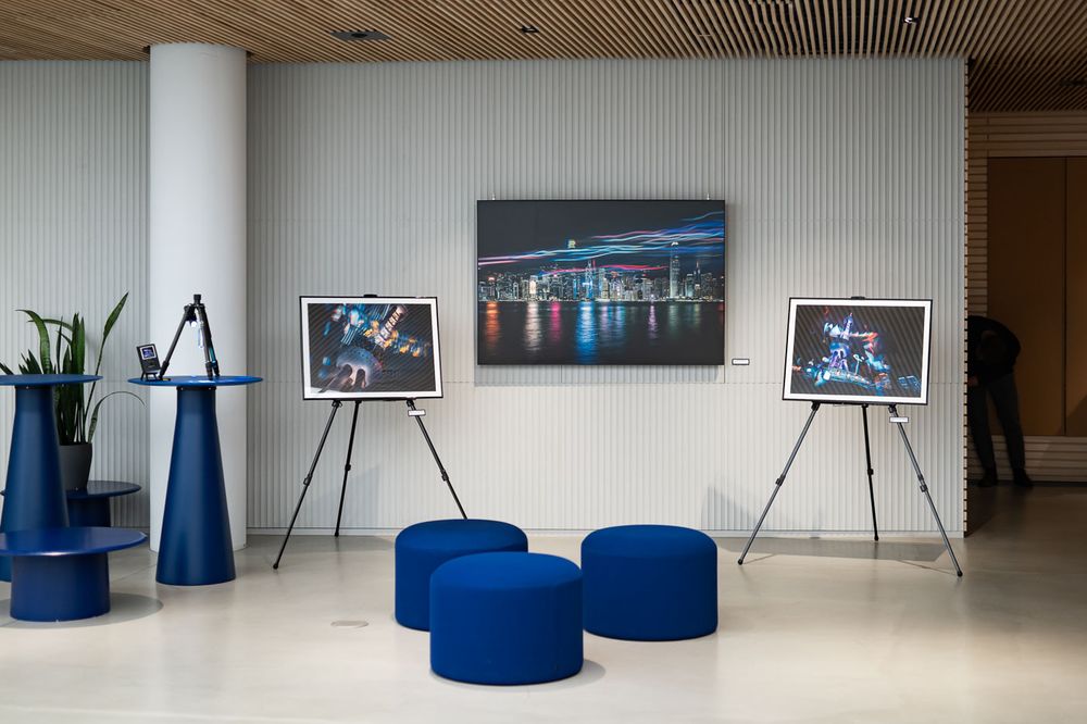 Modern lobby displaying framed cityscape photography on easels with blue ottomans and decorative plants on a polished floor.