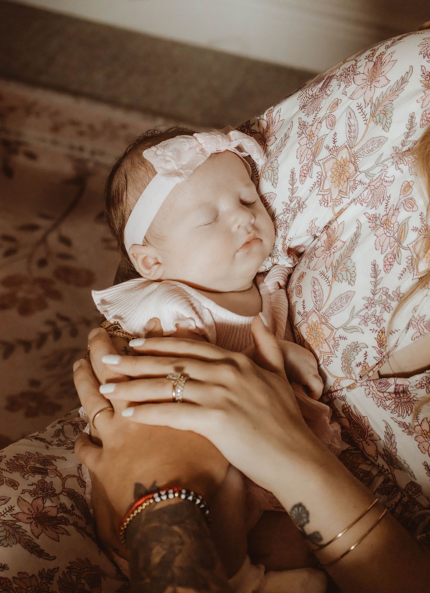 Couple sitting on floor by wooden crib holding newborn baby in floral nursery room.