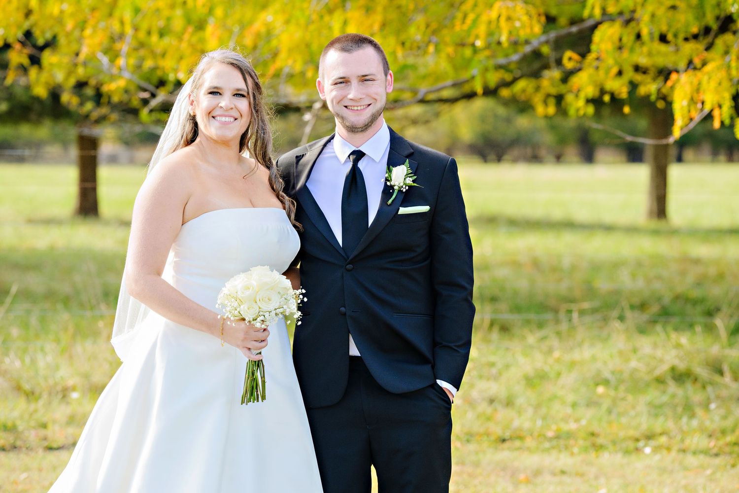 Bride and groom bathed in golden light standing in front of trees with yellow leaves at Kelleys Island Wine Co after their wedding ceremony