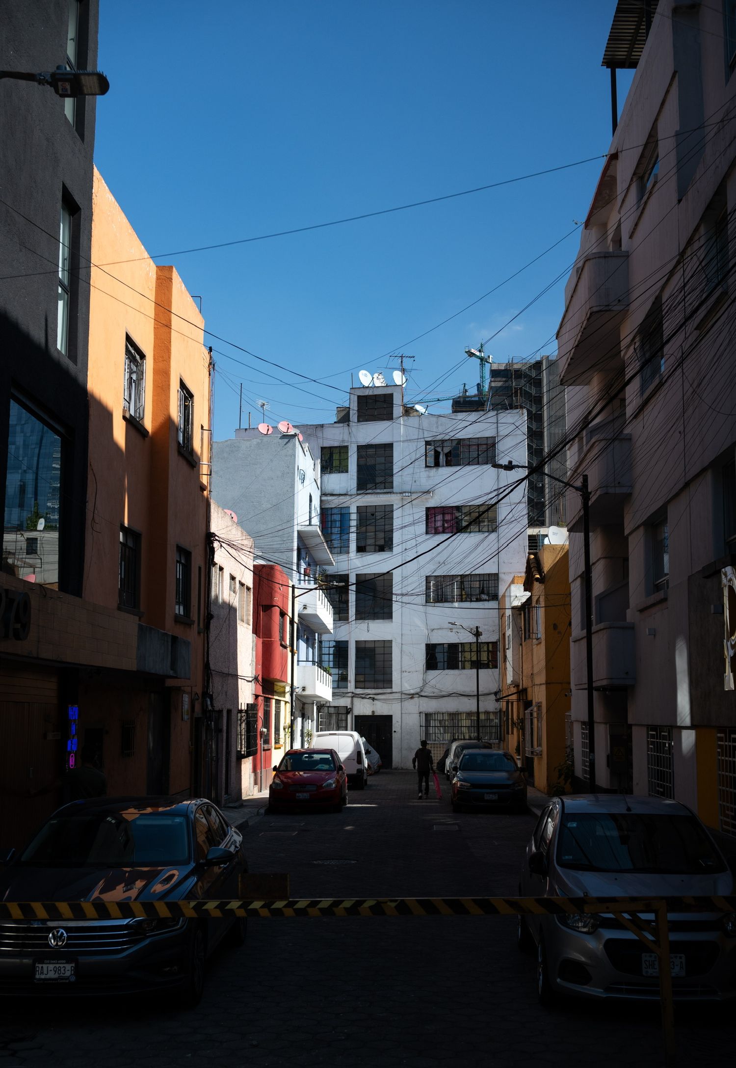 Narrow urban street lined with colorful buildings under a clear blue sky in a Latin American city.