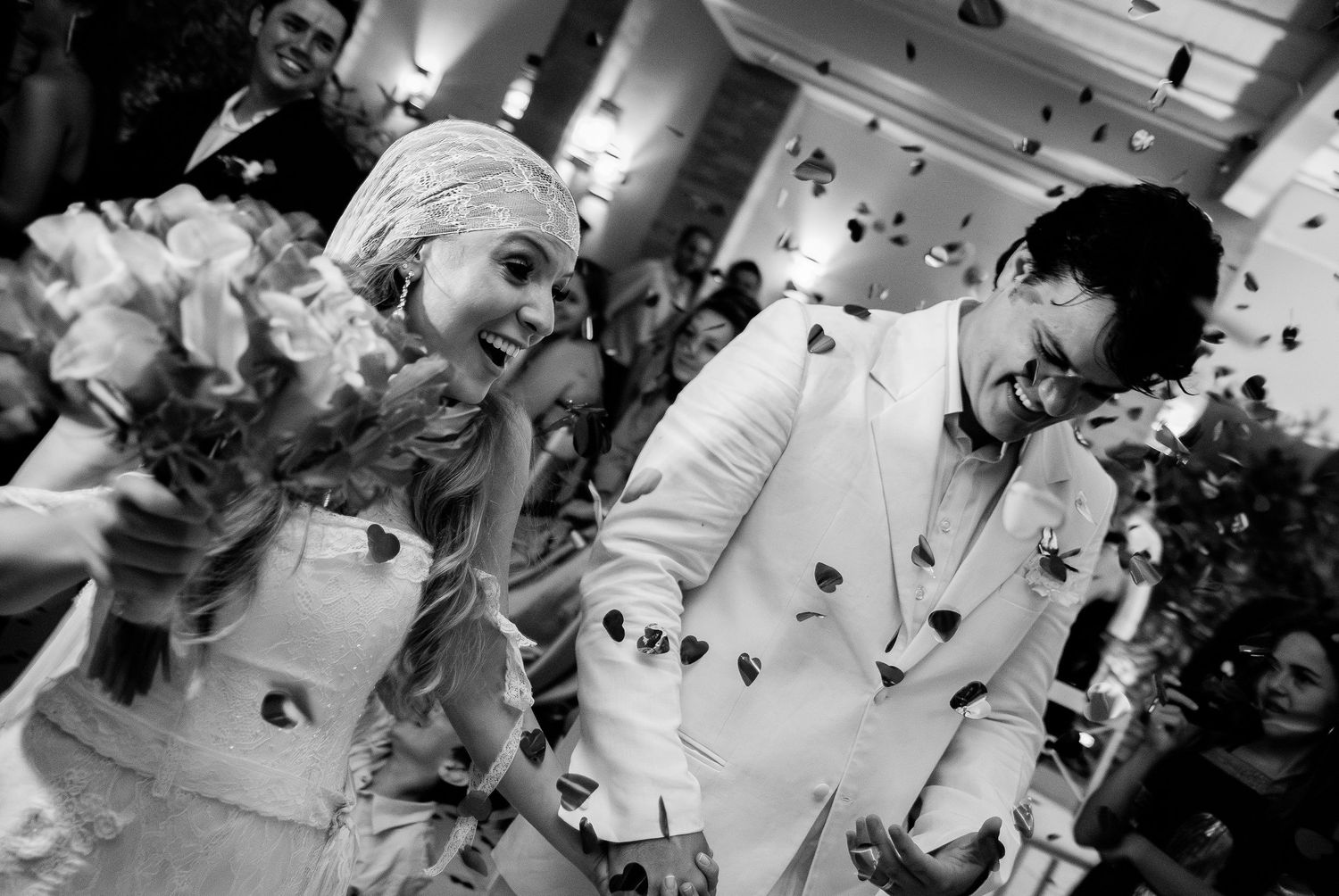Joyful bride and groom laughing as colorful confetti falls during outdoor wedding celebration.