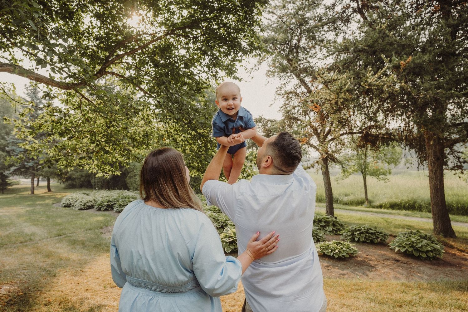 Expecting mother in sage dress interacting with children in spring orchard setting.