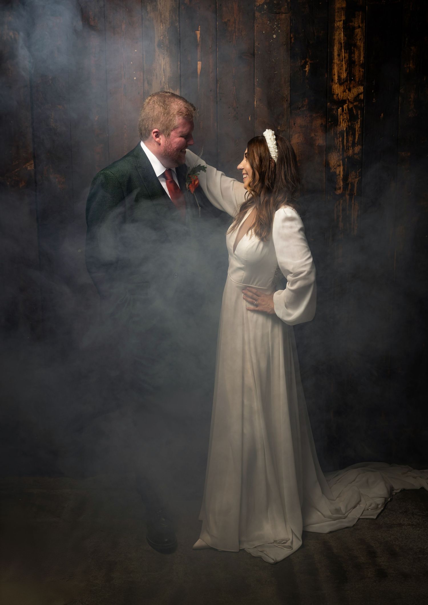Bride and groom share a romantic moment surrounded by atmospheric fog in a rustic dark venue.