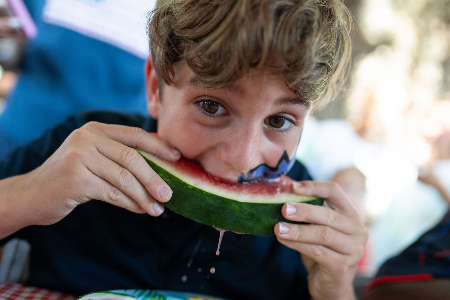 Young boy eagerly eating a fresh slice of watermelon outdoors, juice dripping down his chin.