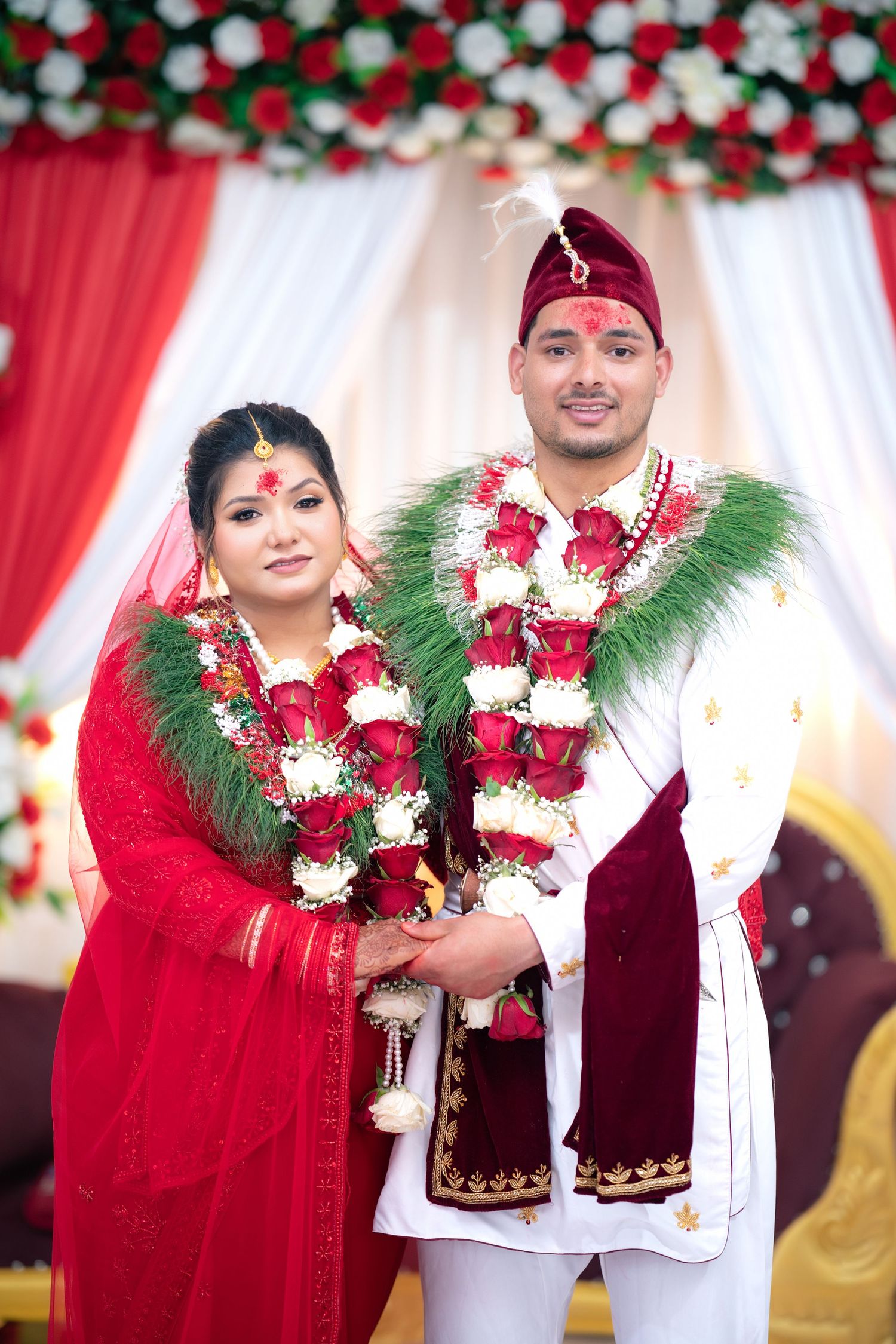 Newlywed couple in traditional Nepali wedding attire with floral garlands posing at decorated mandap.
