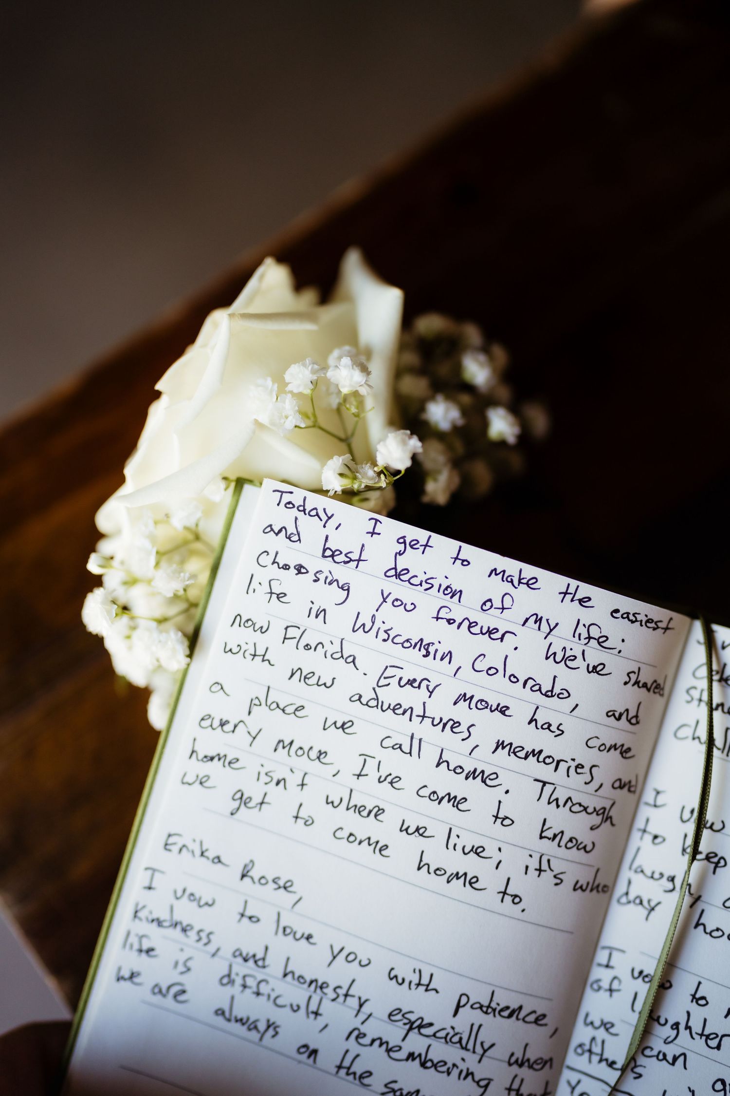 Open wedding vow book with handwritten vows beside white roses and baby's breath flowers.
