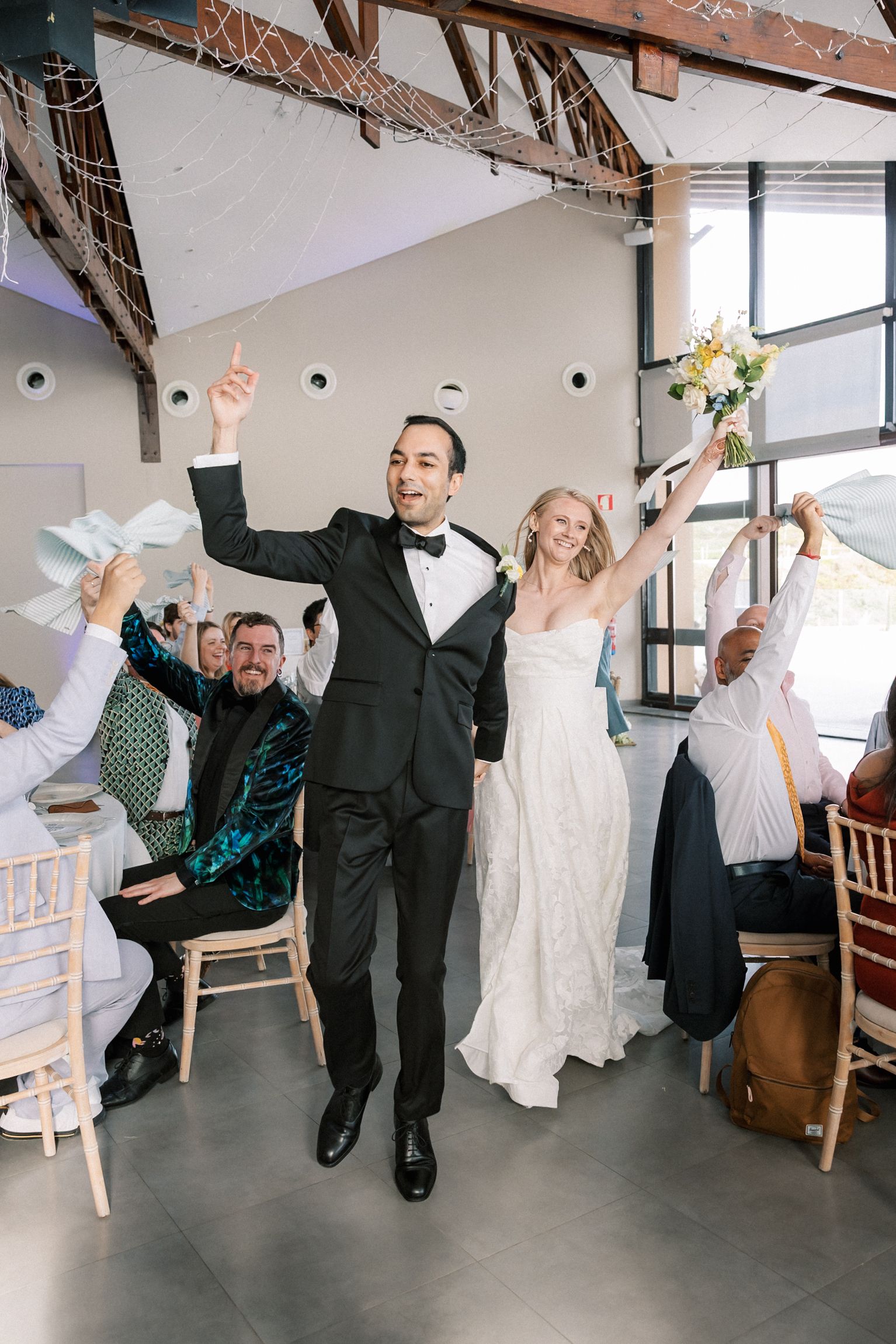 Bride and groom making their joyful entrance into the wedding reception surrounded by cheering guests at Arriba by the Sea in Cascais.