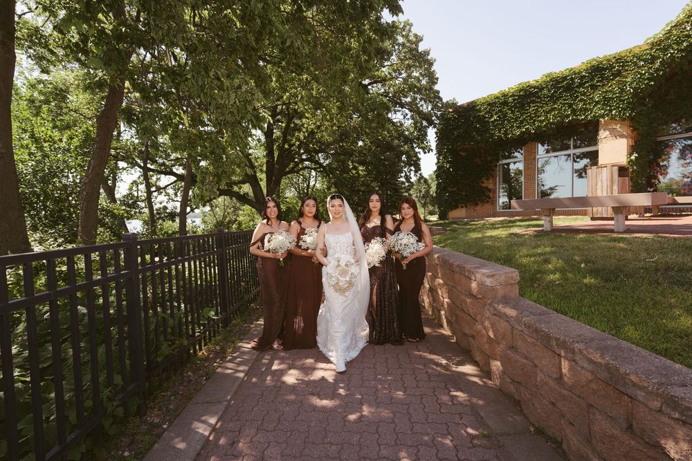 Bride in white gown walks with bridesmaids in brown dresses along brick path at elegant venue.