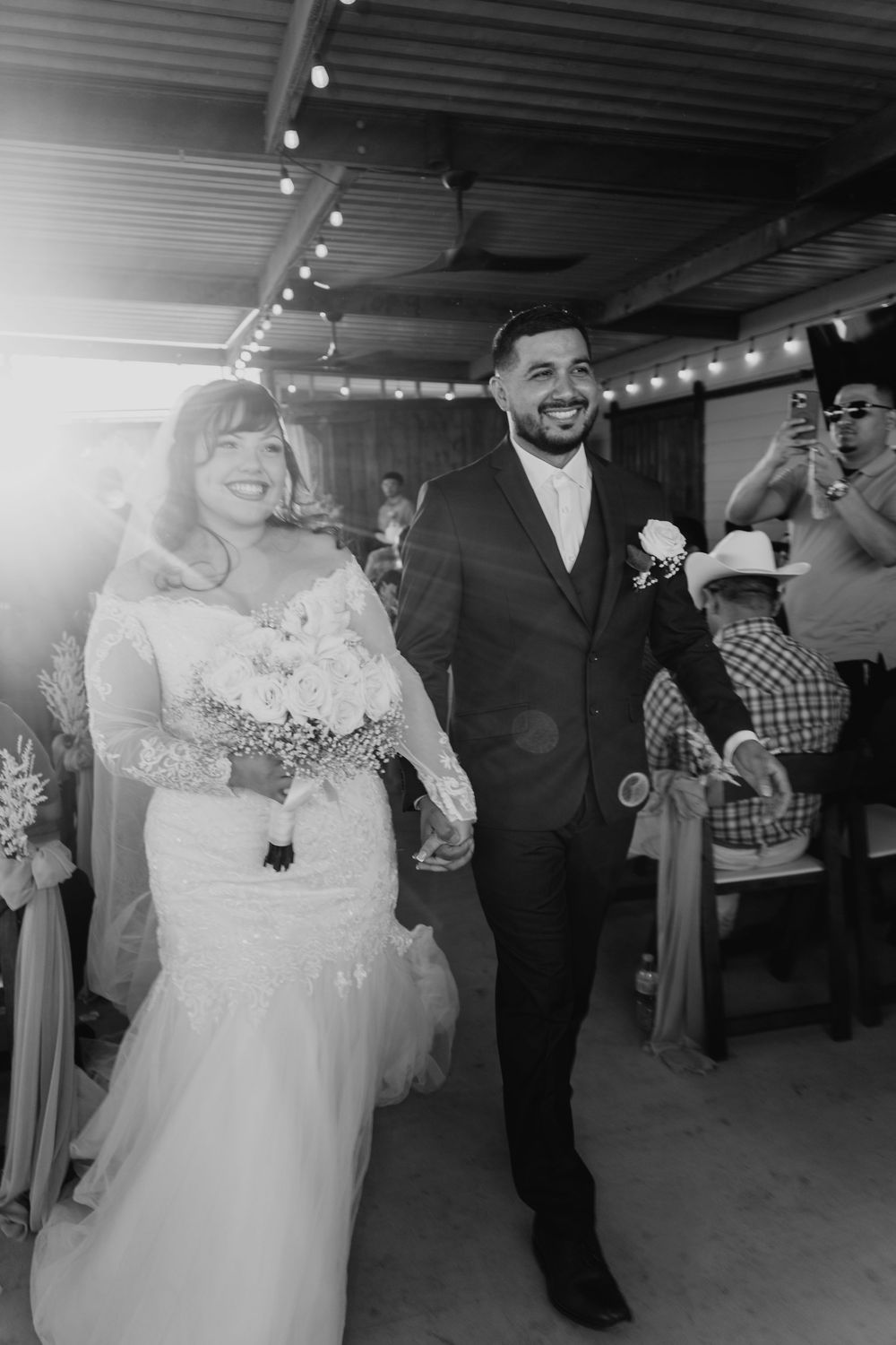 Black and white photo of a smiling bride and groom walking hand in hand at their wedding reception.