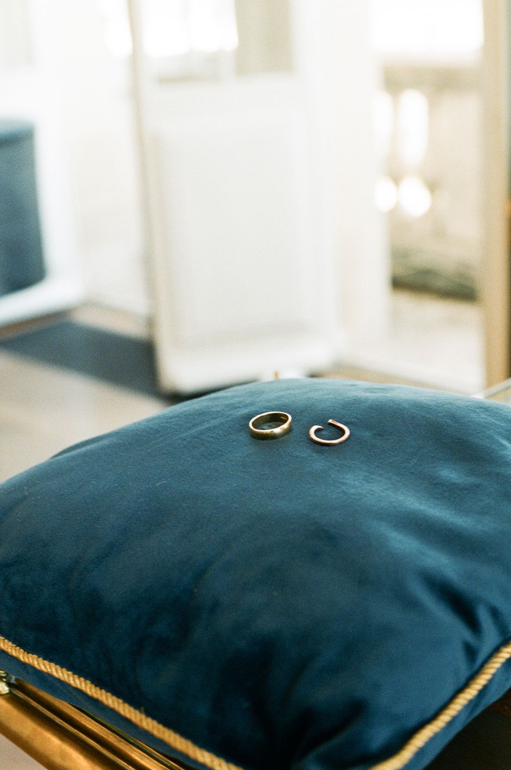 Two gold wedding bands resting on a navy blue velvet pillow with gold trim, with a mirror in the background.
