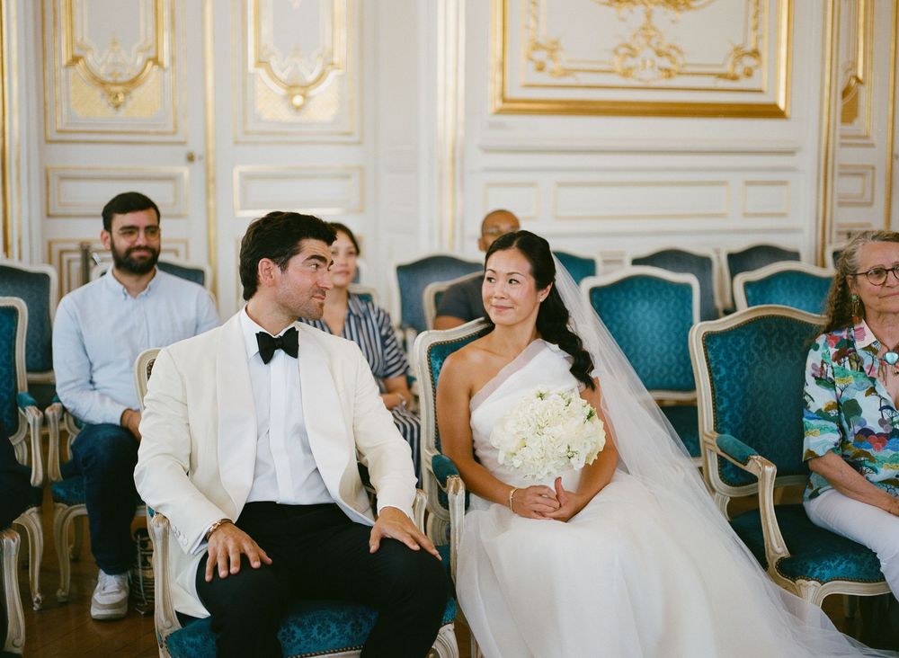 Bride and groom smiling at each other during wedding ceremony in elegant gold room with blue chair. Versailles city hall, Versailles wedding