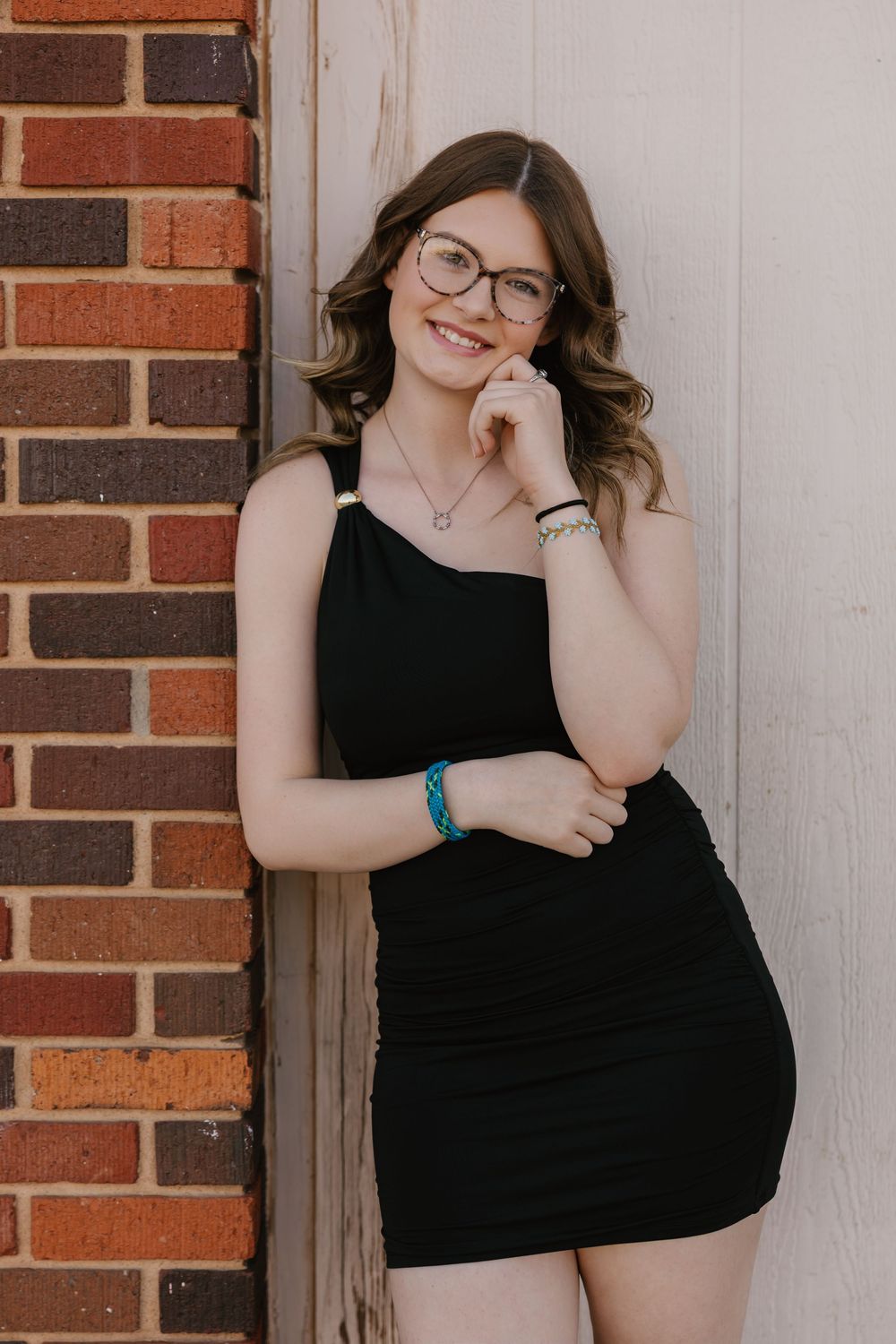 A girl wearing glasses and black dress poses for senior portraits in downtown Tulia, Tx