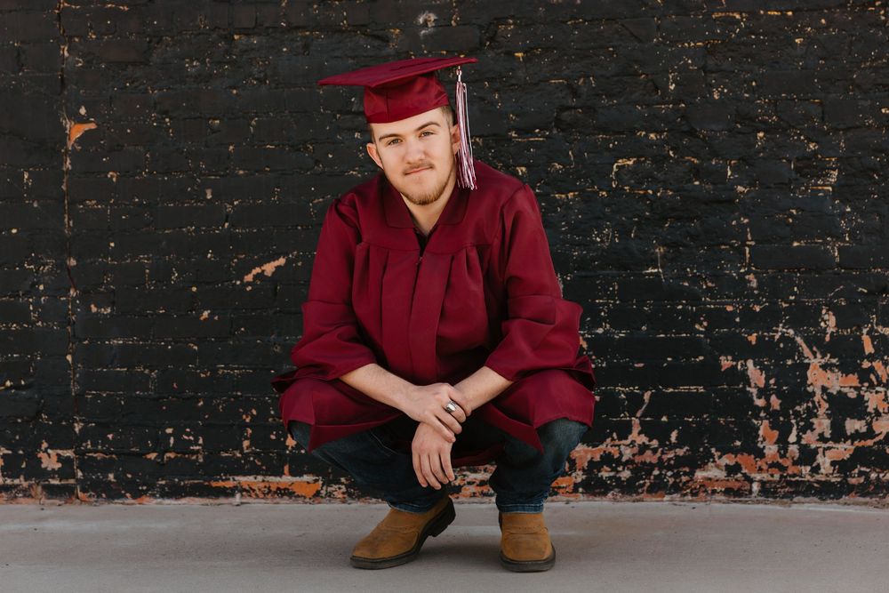 Senior boy wearing his red cap and gown poses for senior portraits in downtown Tulia, Texas
